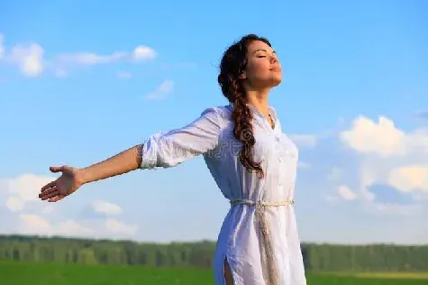 A person standing outdoors with arms open, breathing through the nose
